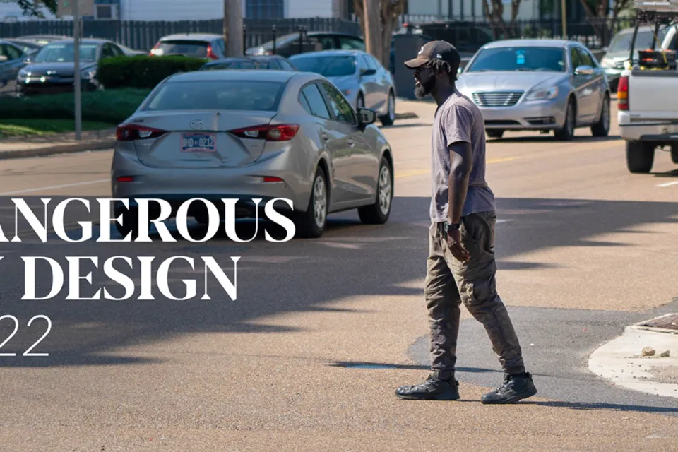Pedestrian crossing street with cars in background and "Dangerous by Design 2022" white font